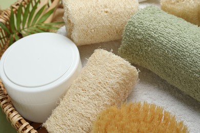 Photo of Natural loofah sponges, cosmetic product, towels, brush and twig in basket, closeup