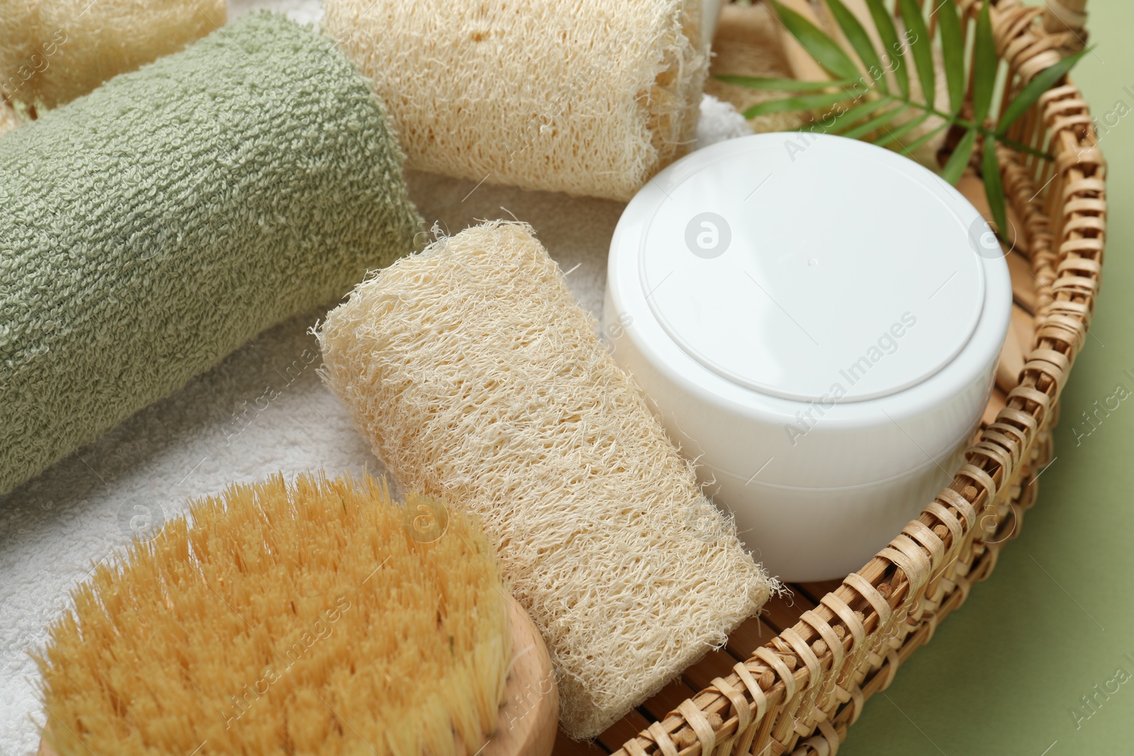 Natural loofah sponges, cosmetic product, towels, brush and twig in basket on green background, closeup Photo of Natural loofah sponges, cosmetic product, towels, brush and twig in basket on green background, closeup
