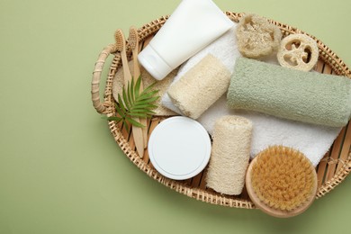 Photo of Natural loofah sponges, cosmetic product, towels, toothbrushes, brush and twig in basket on green background, top view. Space for text