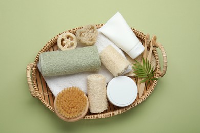Photo of Natural loofah sponges, cosmetic product, towels, toothbrushes, brush and twig in basket on green background, top view