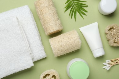 Photo of Natural loofah sponges, cosmetic products, towels, swabs and twig on green background, flat lay