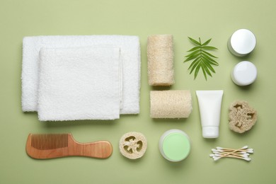 Photo of Natural loofah sponges, cosmetic products, towels, swabs, comb and twig on green background, flat lay