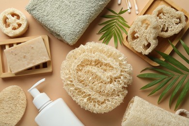 Photo of Natural loofah sponges, towel, soap, cosmetic product, swabs and twigs on beige background, flat lay