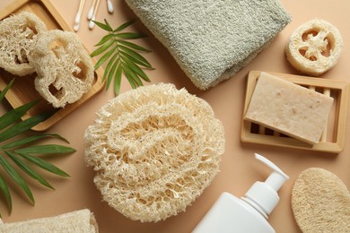 Photo of Natural loofah sponges, towel, soap, cosmetic product, swabs and twigs on beige background, flat lay