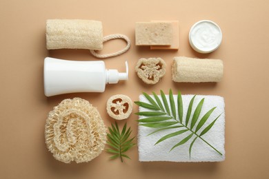 Photo of Natural loofah sponges, cosmetic products, towel and twigs on beige background, flat lay