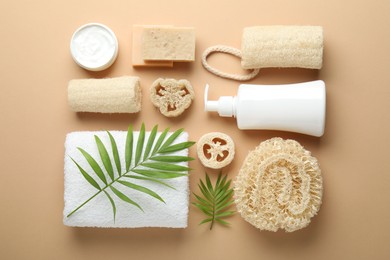 Photo of Natural loofah sponges, cosmetic products, towel and twigs on beige background, flat lay