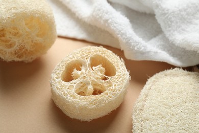Photo of Natural loofah sponges and towel on beige background, closeup