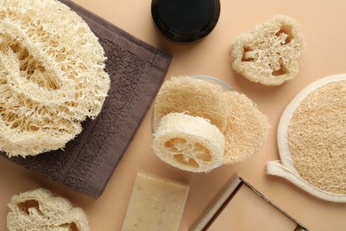 Photo of Natural loofah sponges, cosmetic product, towel and soap on beige background, flat lay