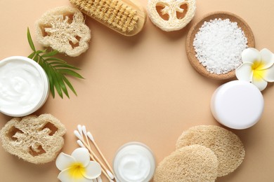 Photo of Frame of natural loofah sponges, cosmetic products, swabs, plumeria flowers, brush and green twig on beige background, flat lay. Space for text