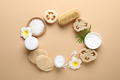 Photo of Frame of natural loofah sponges, cosmetic products, swabs, plumeria flowers, brush and green twig on beige background, flat lay. Space for text