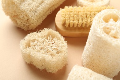 Photo of Natural loofah sponges and brush on beige background, closeup
