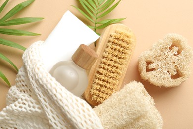 Photo of Natural loofah sponges, cosmetic products, brush and green twigs on beige background, flat lay