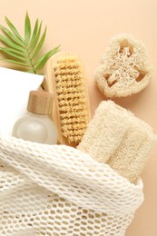 Photo of Natural loofah sponges, cosmetic products, brush and green twig on beige background, flat lay