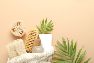 Photo of Natural loofah sponges, cosmetic products, brush and green twigs on beige background, flat lay