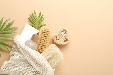 Photo of Natural loofah sponges, cosmetic products, brush and green twigs on beige background, flat lay. Space for text