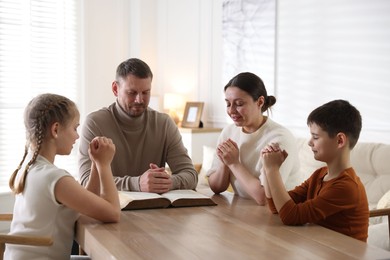 Photo of Family with Bible praying at table indoors