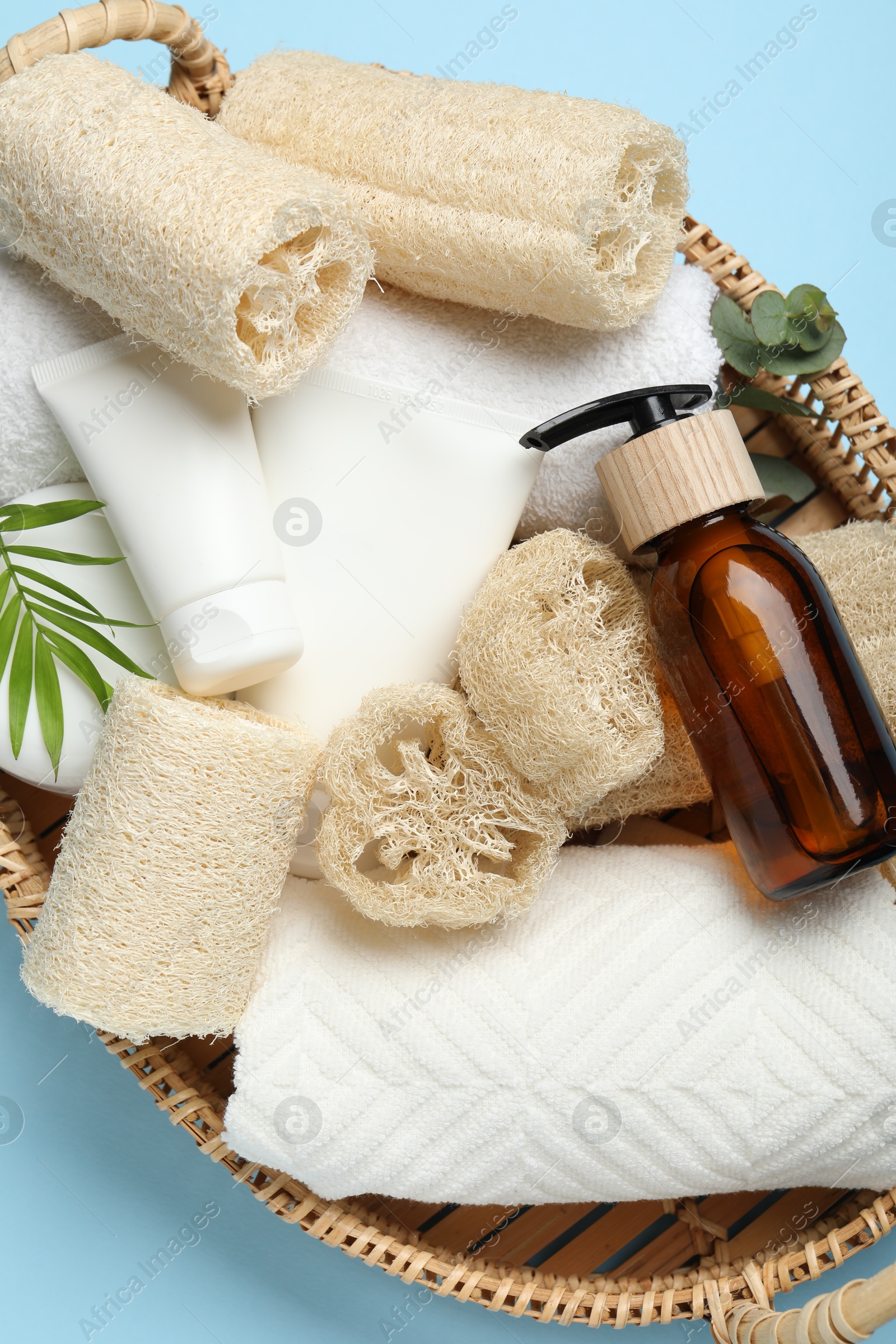 Natural loofah sponges, towels, cosmetic products and green twig in basket on light blue background, top view Photo of Natural loofah sponges, towels, cosmetic products and green twig in basket on light blue background, top view