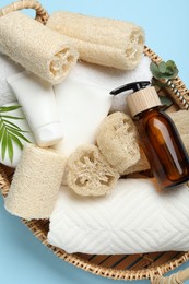Photo of Natural loofah sponges, towels, cosmetic products and green twig in basket on light blue background, top view