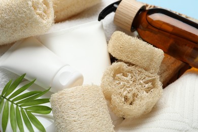 Photo of Natural loofah sponges, towels, cosmetic products and green twig in basket, closeup