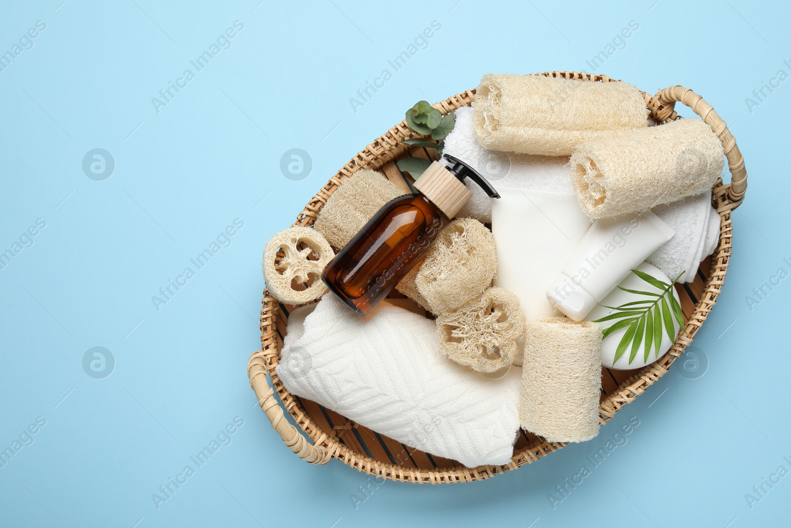 Natural loofah sponges, towels, cosmetic products and floral decor in basket on light blue background, top view. Space for text Photo of Natural loofah sponges, towels, cosmetic products and floral decor in basket on light blue background, top view. Space for text