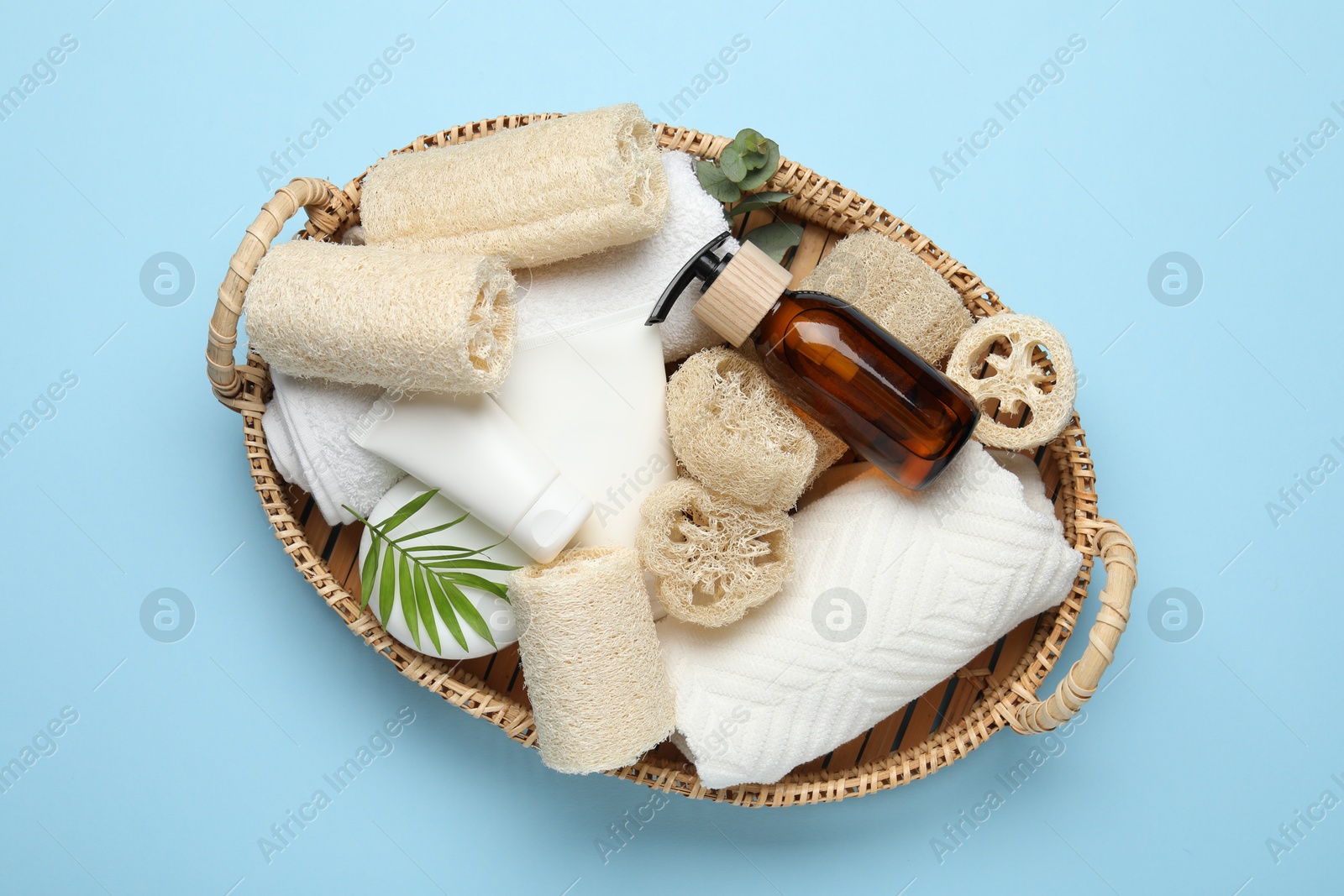 Natural loofah sponges, towels, cosmetic products and floral decor in basket on light blue background, top view Photo of Natural loofah sponges, towels, cosmetic products and floral decor in basket on light blue background, top view