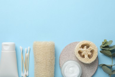 Photo of Natural loofah sponges, cosmetic products, swabs and eucalyptus branch on light blue background, flat lay. Space for text
