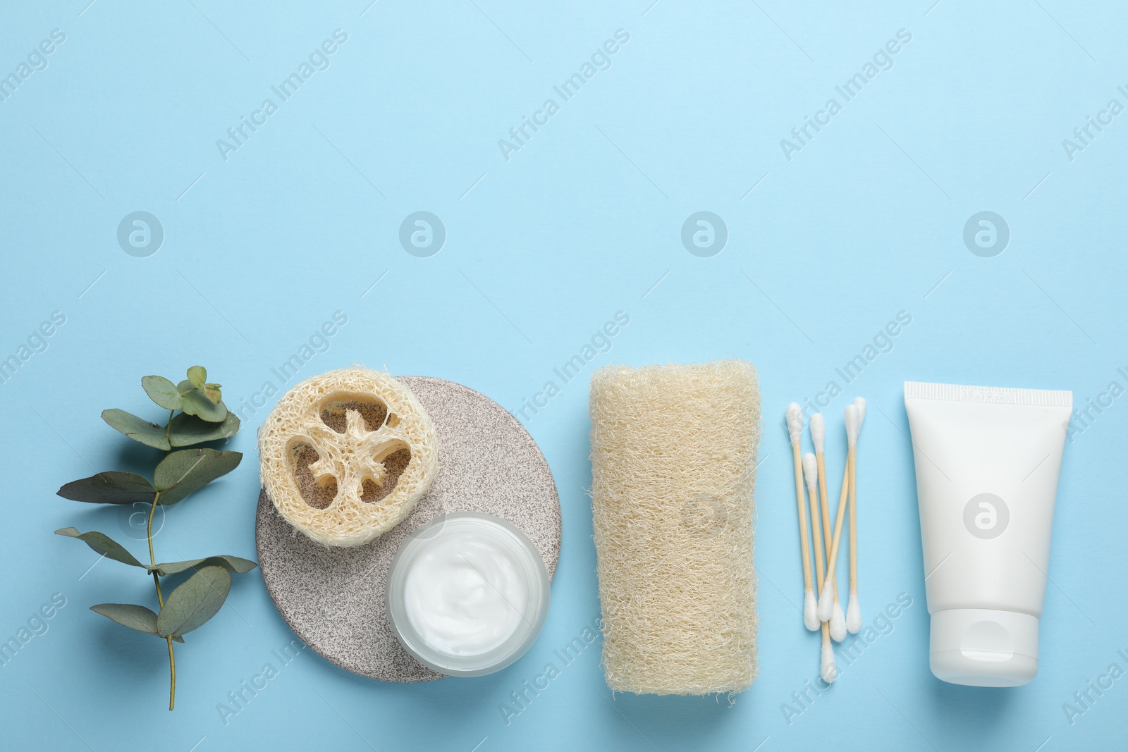 Natural loofah sponges, cosmetic products, swabs and eucalyptus branch on light blue background, flat lay. Space for text Photo of Natural loofah sponges, cosmetic products, swabs and eucalyptus branch on light blue background, flat lay. Space for text