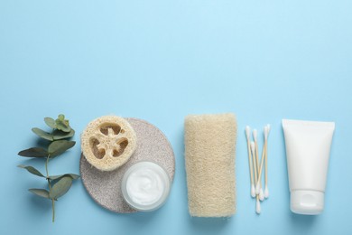 Photo of Natural loofah sponges, cosmetic products, swabs and eucalyptus branch on light blue background, flat lay. Space for text