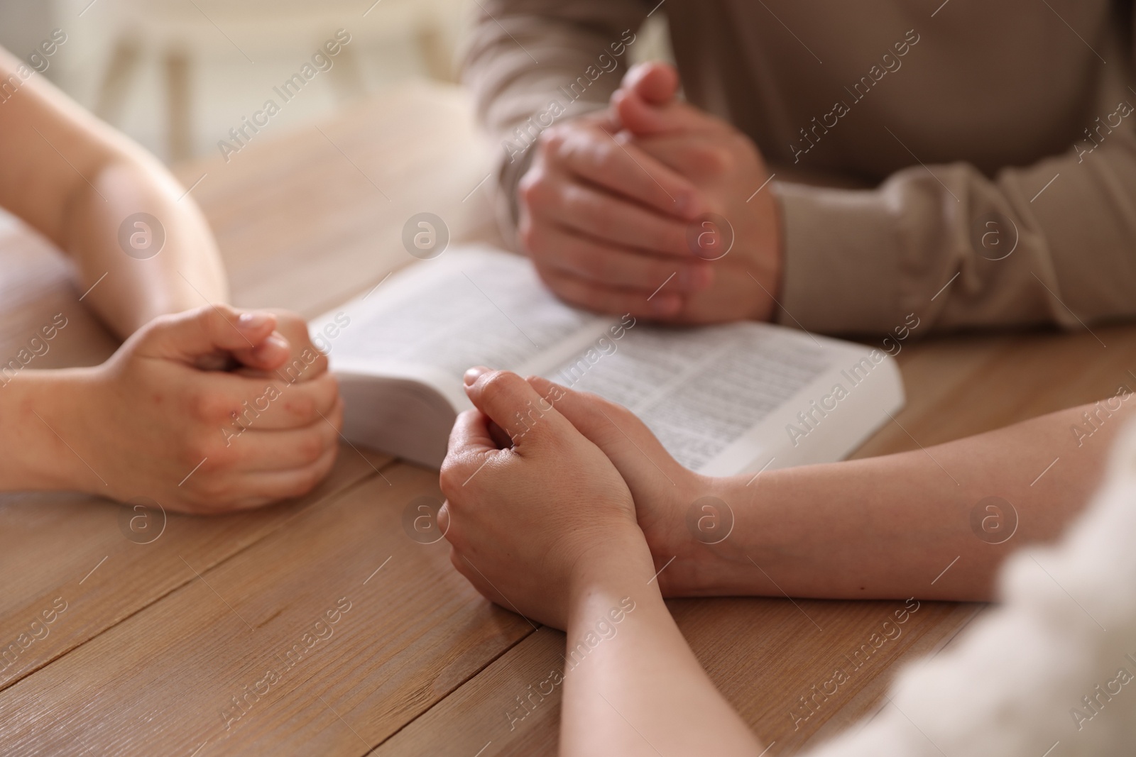 Family with Bible praying at table indoors, closeup Photo of Family with Bible praying at table indoors, closeup