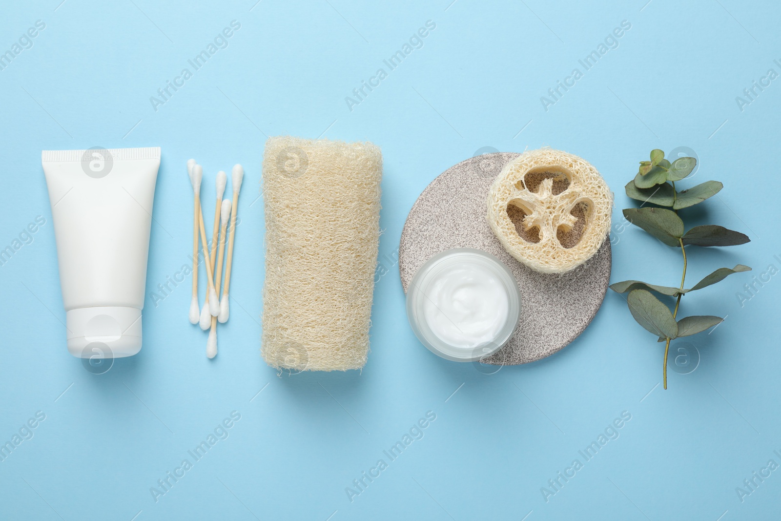 Natural loofah sponges, cosmetic products, swabs and eucalyptus branch on light blue background, flat lay Photo of Natural loofah sponges, cosmetic products, swabs and eucalyptus branch on light blue background, flat lay