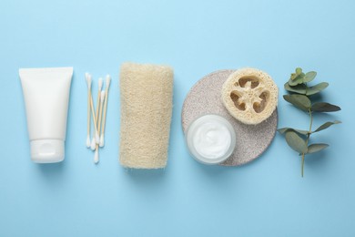 Photo of Natural loofah sponges, cosmetic products, swabs and eucalyptus branch on light blue background, flat lay