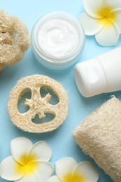 Photo of Natural loofah sponges, cosmetic products and plumeria flowers on light blue background, flat lay