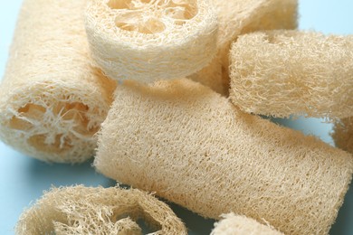 Photo of Natural loofah sponges on light blue background, closeup
