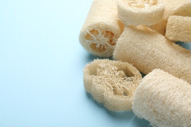 Photo of Natural loofah sponges on light blue background, closeup. Space for text
