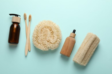 Photo of Natural loofah sponges, cosmetic products and toothbrushes on light blue background, flat lay