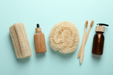 Photo of Natural loofah sponges, cosmetic products and toothbrushes on light blue background, flat lay