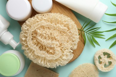 Photo of Natural loofah sponges, cosmetic products and green twigs on light blue background, flat lay