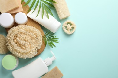 Photo of Natural loofah sponges, cosmetic products and green twigs on light blue background, flat lay. Space for text