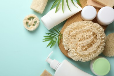 Photo of Natural loofah sponges, cosmetic products and green twigs on light blue background, flat lay. Space for text