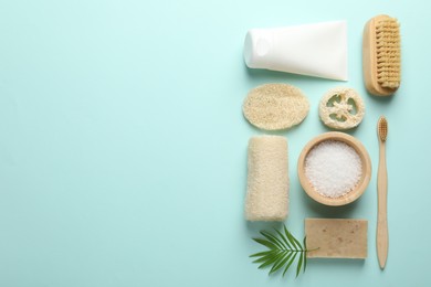Photo of Natural loofah sponges, cosmetic products, brush, toothbrush and green twig on light blue background, flat lay. Space for text