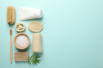 Photo of Natural loofah sponges, cosmetic products, brush, toothbrush and green twig on light blue background, flat lay. Space for text