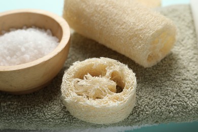 Photo of Natural loofah sponges, sea salt and towel on table, closeup
