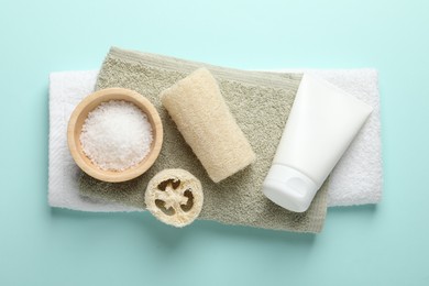 Photo of Natural loofah sponges, cosmetic products and towels on light blue background, top view