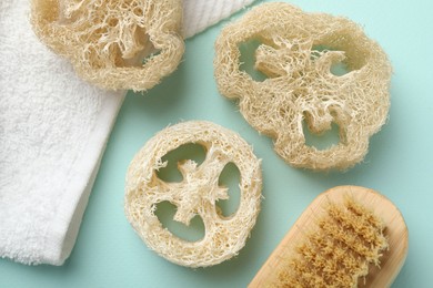 Photo of Natural loofah sponges, brush and towel on light blue background, flat lay