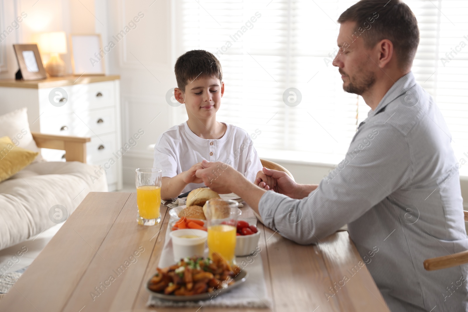 Father and son praying before dinner at table indoors Photo of Father and son praying before dinner at table indoors
