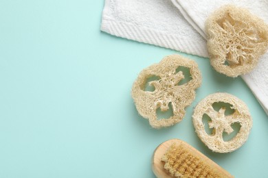 Photo of Natural loofah sponges, brush and towel on light blue background, flat lay. Space for text