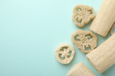 Photo of Natural loofah sponges on light blue background, flat lay. Space for text
