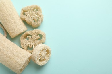Photo of Natural loofah sponges on light blue background, flat lay. Space for text