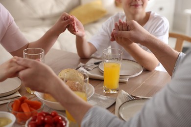 Photo of Family praying together before dinner at table indoors, closeup