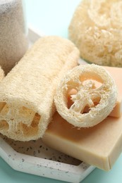 Photo of Natural loofah sponges and soap on light blue background, closeup